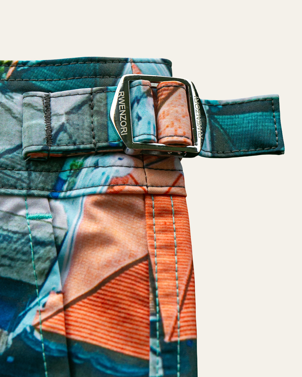 Close-up of the stainless steel buckle hardware on RWENZORI Bali photo print swim shorts.