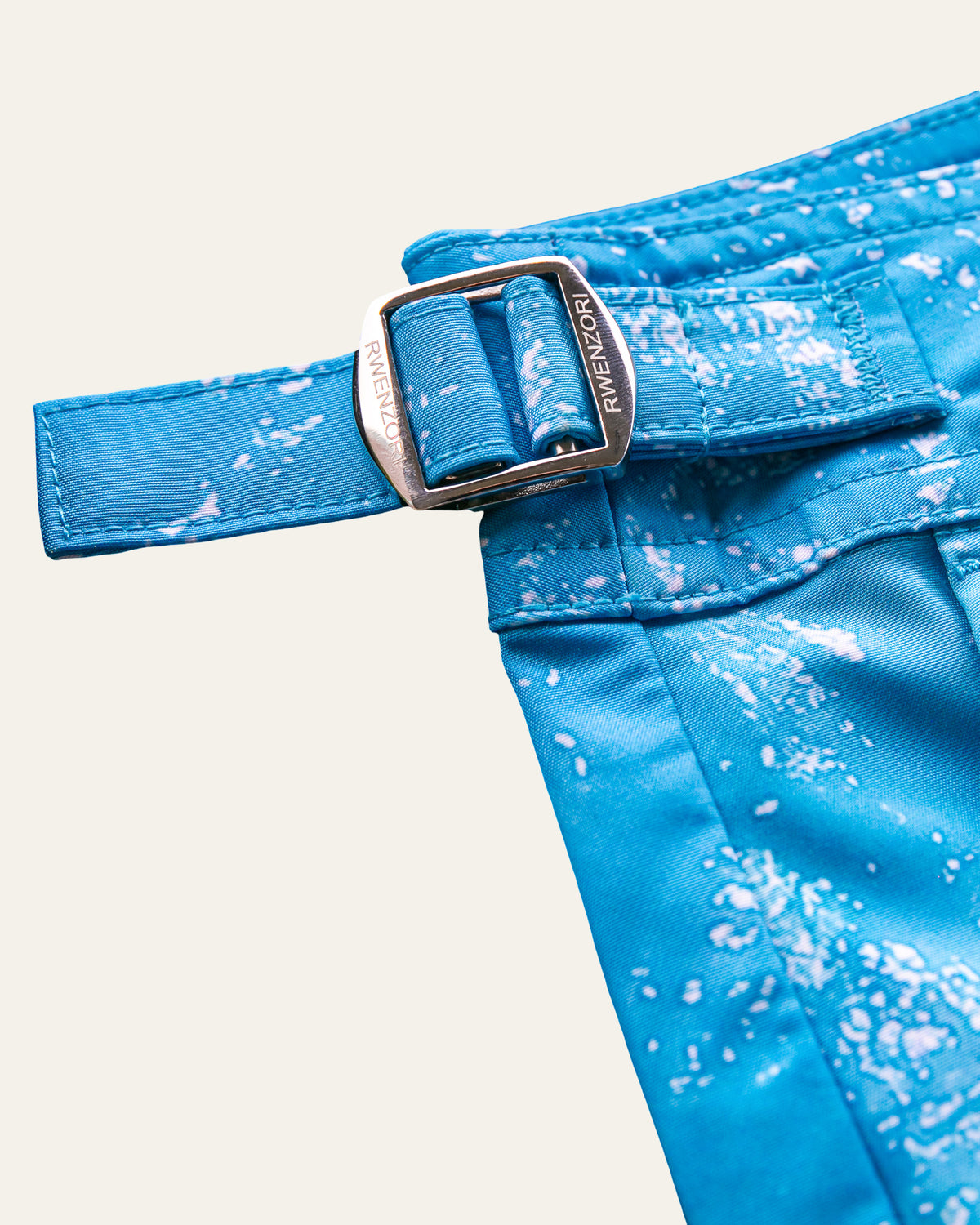 Close-up of the stainless steel buckle hardware on RWENZORI French Riviera photo print swim shorts.