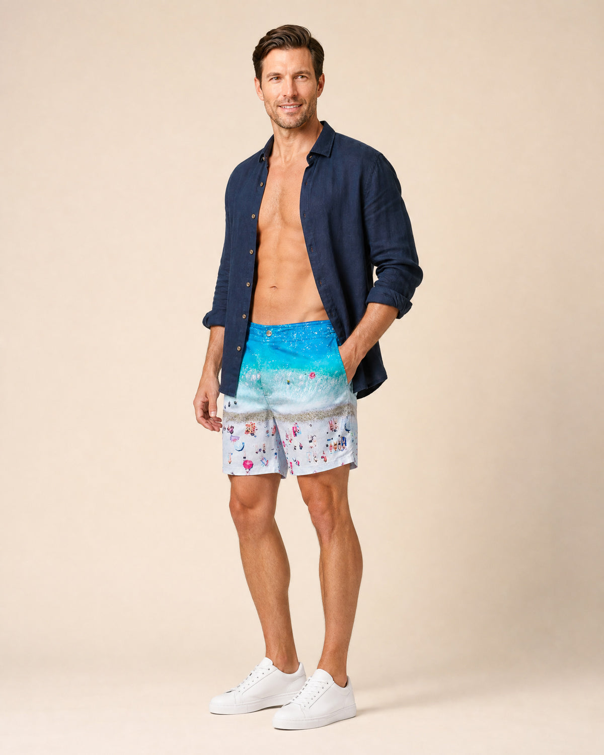 Man wearing RWENZORI French Riviera photo print swim trunks with an open navy linen resort shirt.
