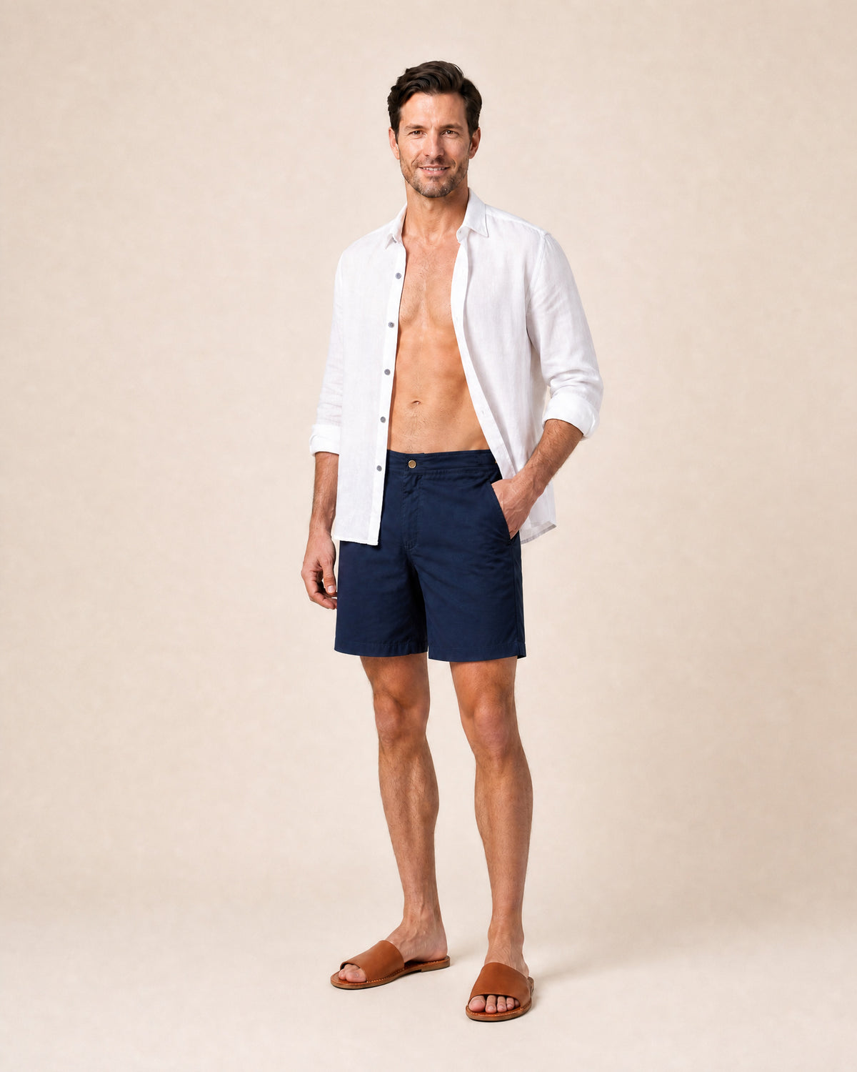 Man wearing RWENZORI Performance Series Swim Shorts Nautic Navy with white linen resort shirt open with leather slides.
