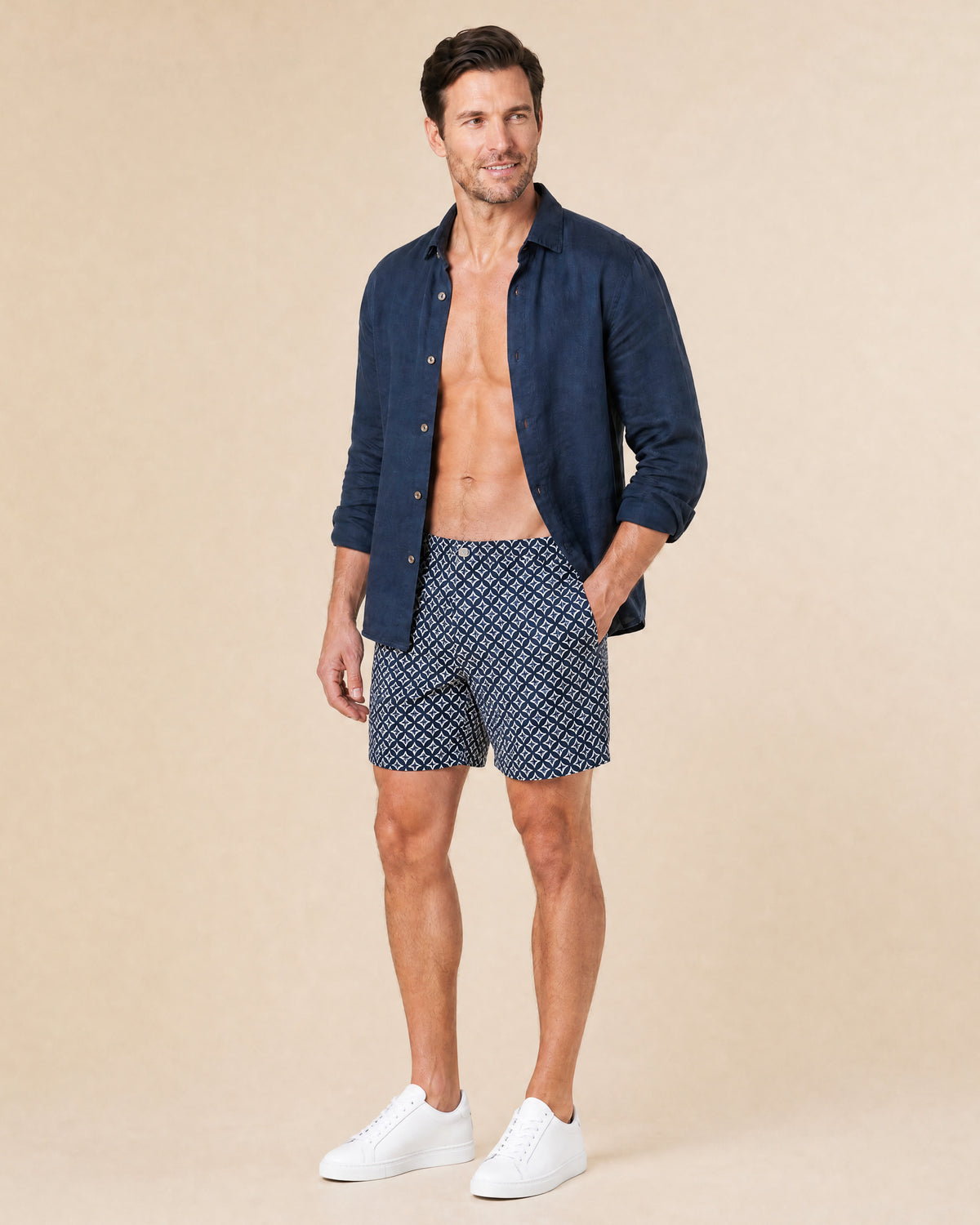 Man wearing RWENZORI Palladio Venezia diamond print swim shorts with an open navy linen resort shirt.