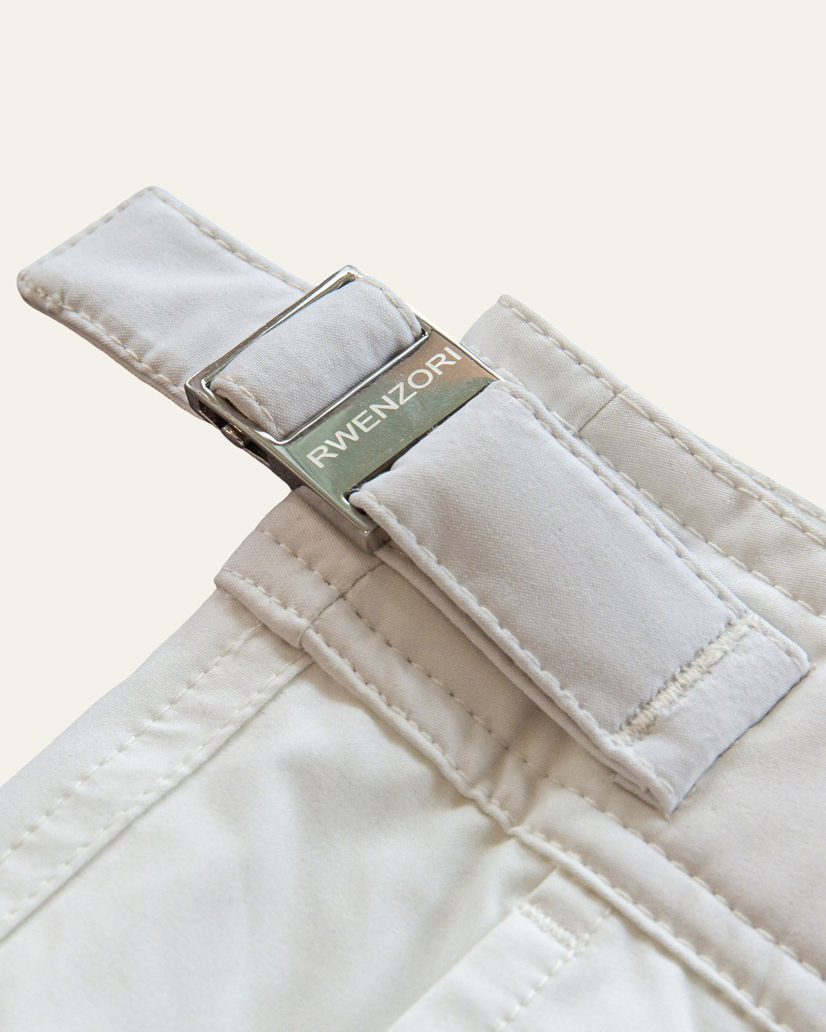 Close-up of the stainless steel buckle hardware on RWENZORI Riviera White Performance Series swim shorts.