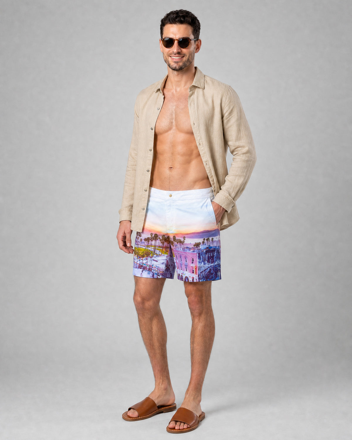 Man wearing RWENZORI Venice Beach photo print swim shorts with an open linen taupe resort shirt.