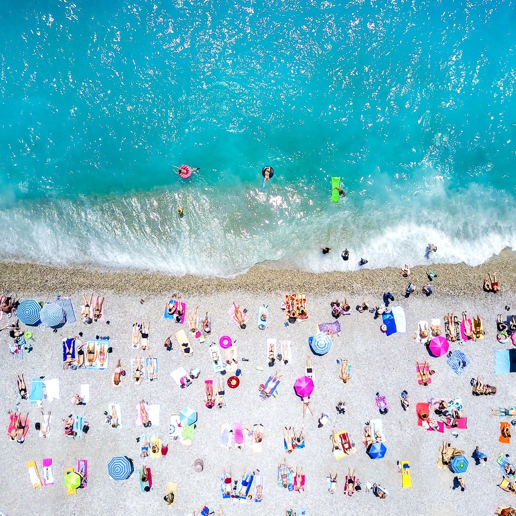 Aerial view of a crowded sandy beach in the French Riviera, France with turquoise ocean water, people swimming and relaxing, and many colorful umbrellas and lounge chairs.