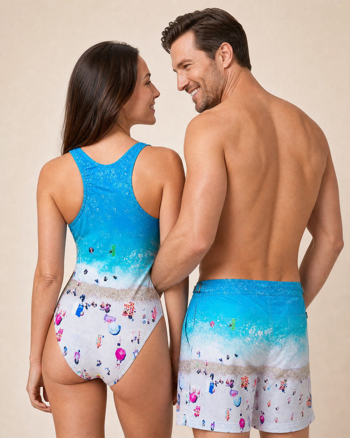 Couple in matching RWENZORI swimwear, rear view — she wears the French Riviera print MATCH HIM one-piece swimsuit.