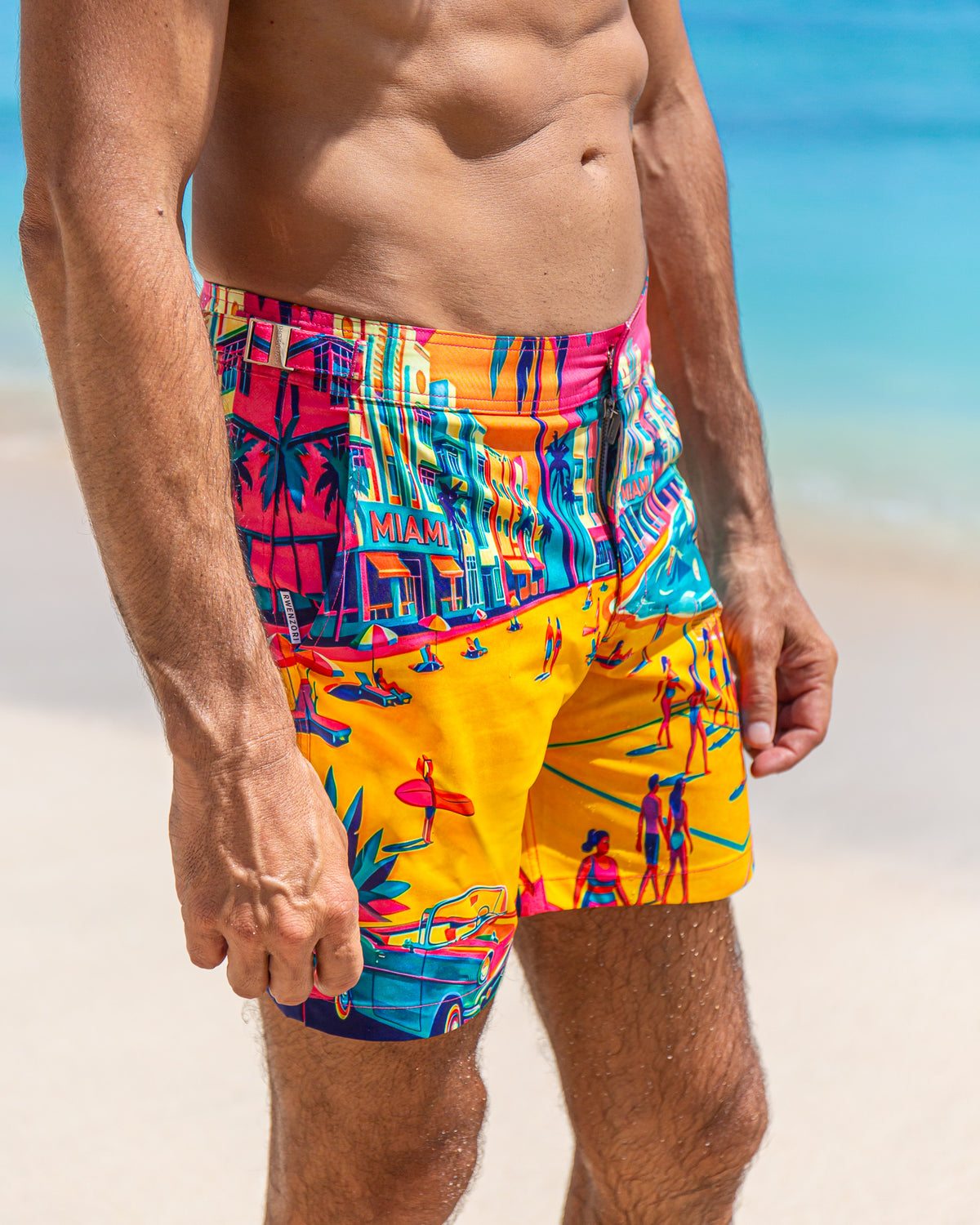 Man wearing RWENZORI Miami photo print swim trunks closeup side view at the beach.