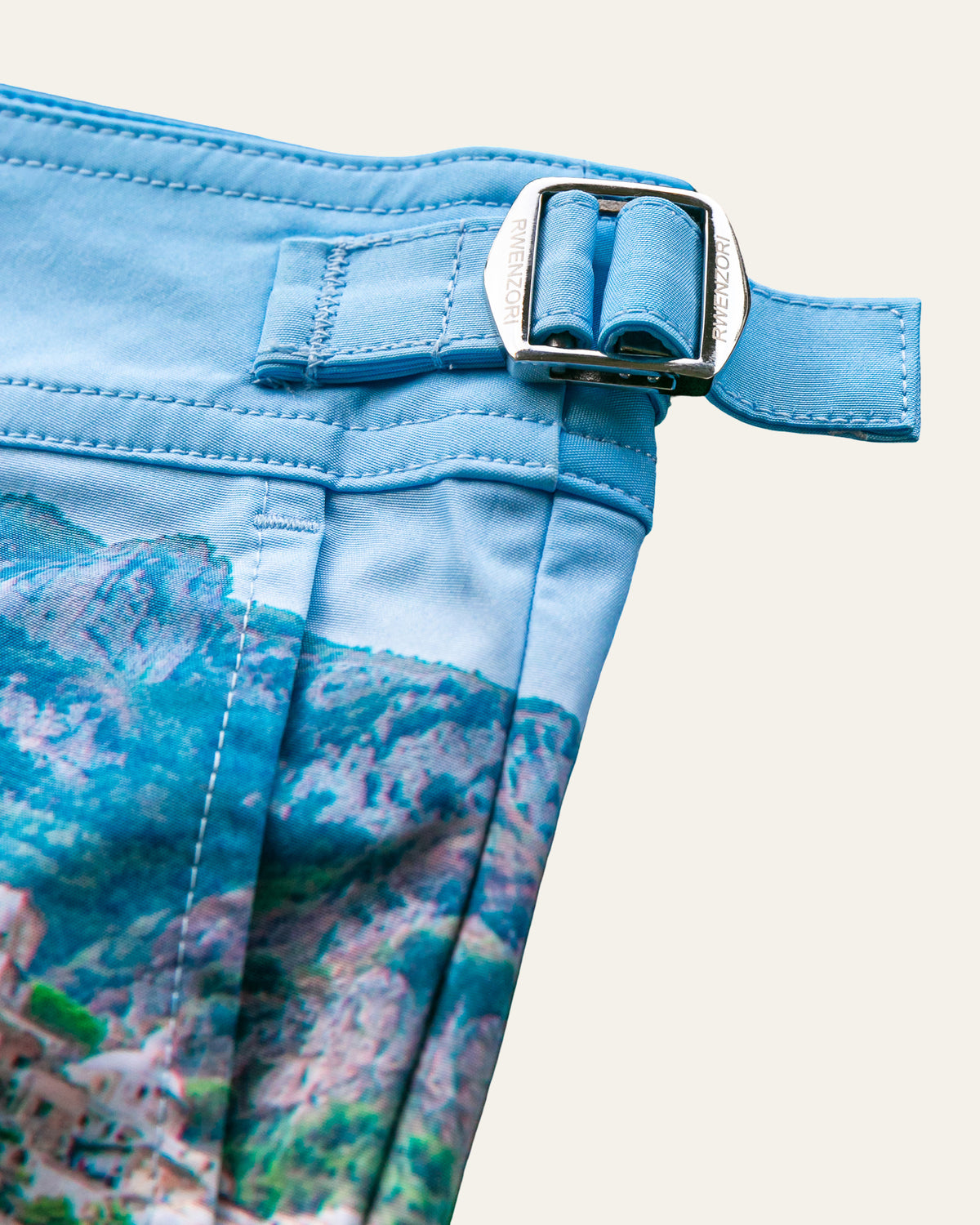 Close-up of the stainless steel buckle hardware on RWENZORI Positano photo print swim shorts.