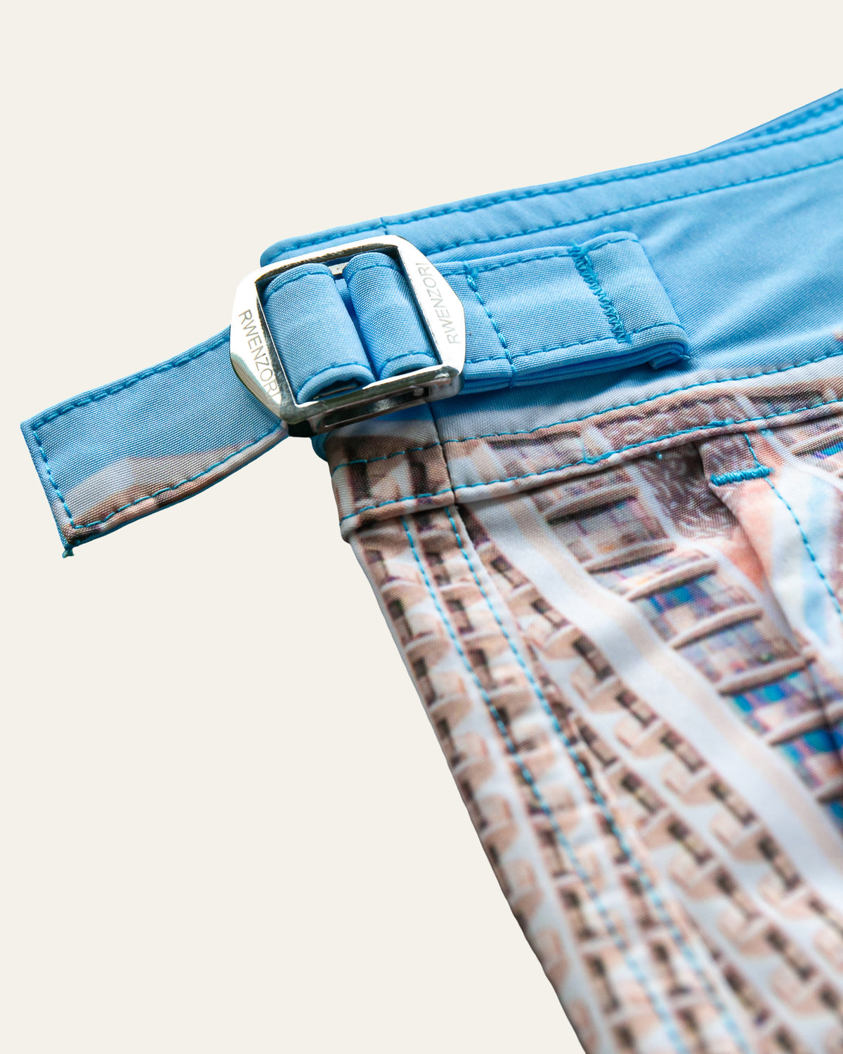 Close-up of the stainless steel buckle hardware on RWENZORI Waikiki photo print swim shorts.