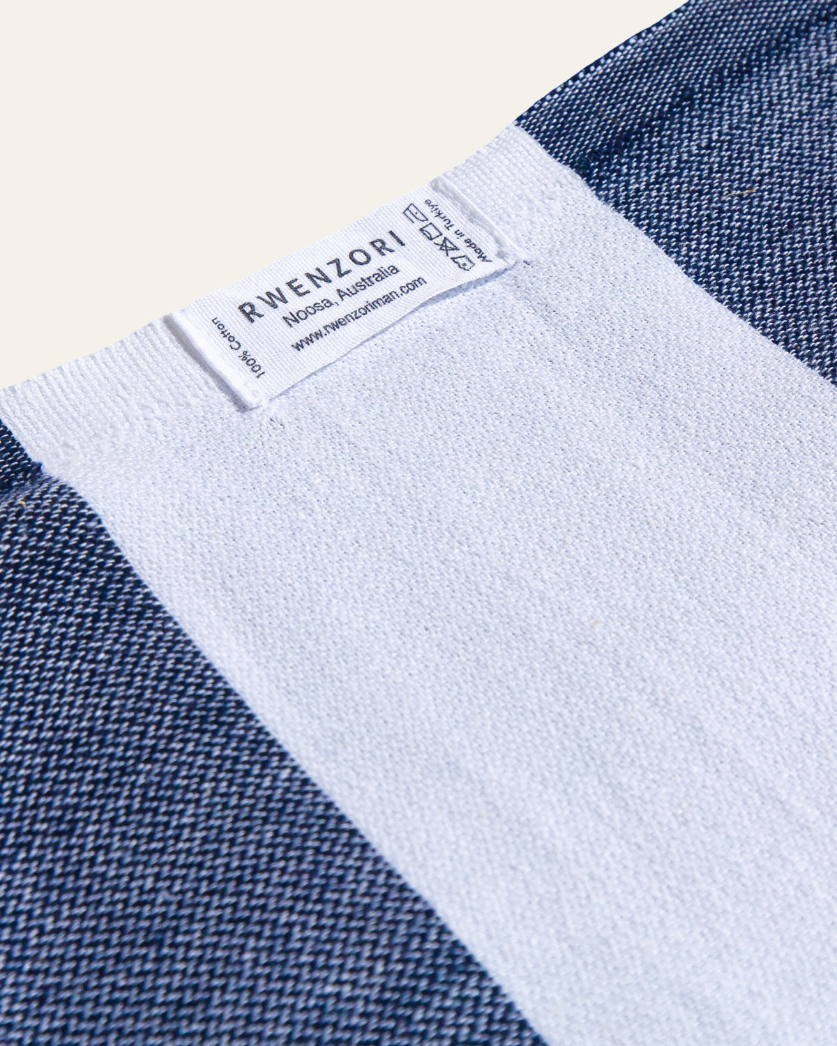 Close-up of a garment's neck area showing a white inner collar and a sewn-in label that reads RWENZORI, with navy blue and white woven fabric visible around it.